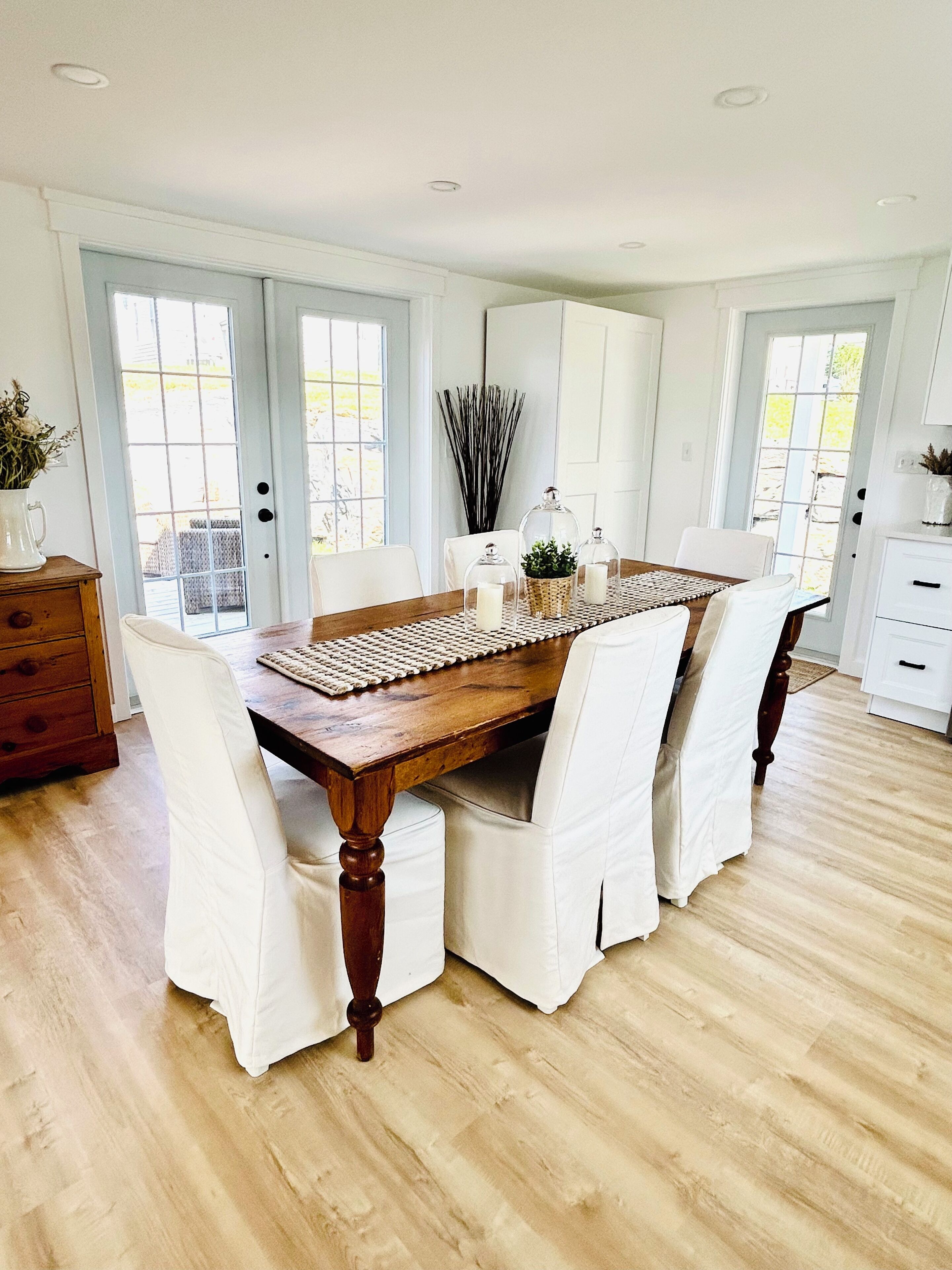 A dining area with a wooden table, white upholstered chairs, and a woven placemat.
