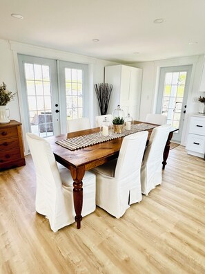 Een eetruimte met een houten tafel, witte gestoffeerde stoelen en een geweven placemat.