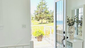 A bright hallway with a wooden floor leading to a glass door opening to a balcony with a potted plant and a tree. - Coastal Gale (Lunenburg)