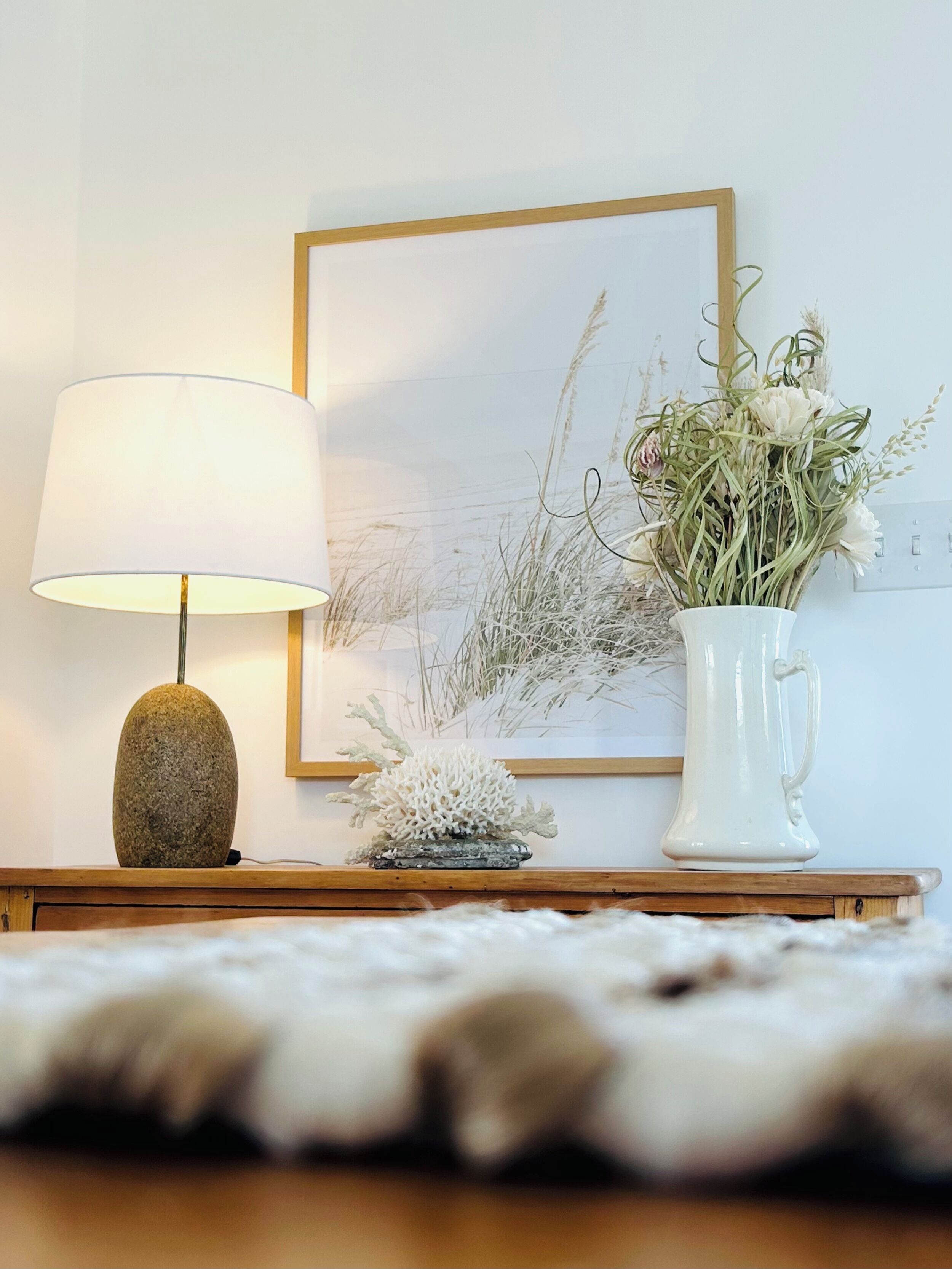 A lamp, a vase with flowers, and a framed picture on a wooden table.