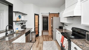 Una cocina moderna con armarios blancos, encimeras de granito, una estufa negra y una puerta de madera que da a otra habitación.
