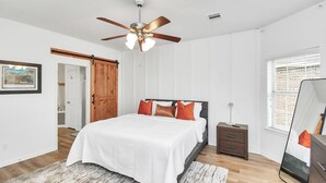 Un dormitorio con cama, mesita de noche, cómoda, ventilador de techo y ventana con persianas.