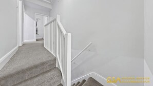 Un escalier avec une rampe blanche et des marches recouvertes de moquette, menant à une porte située en haut.