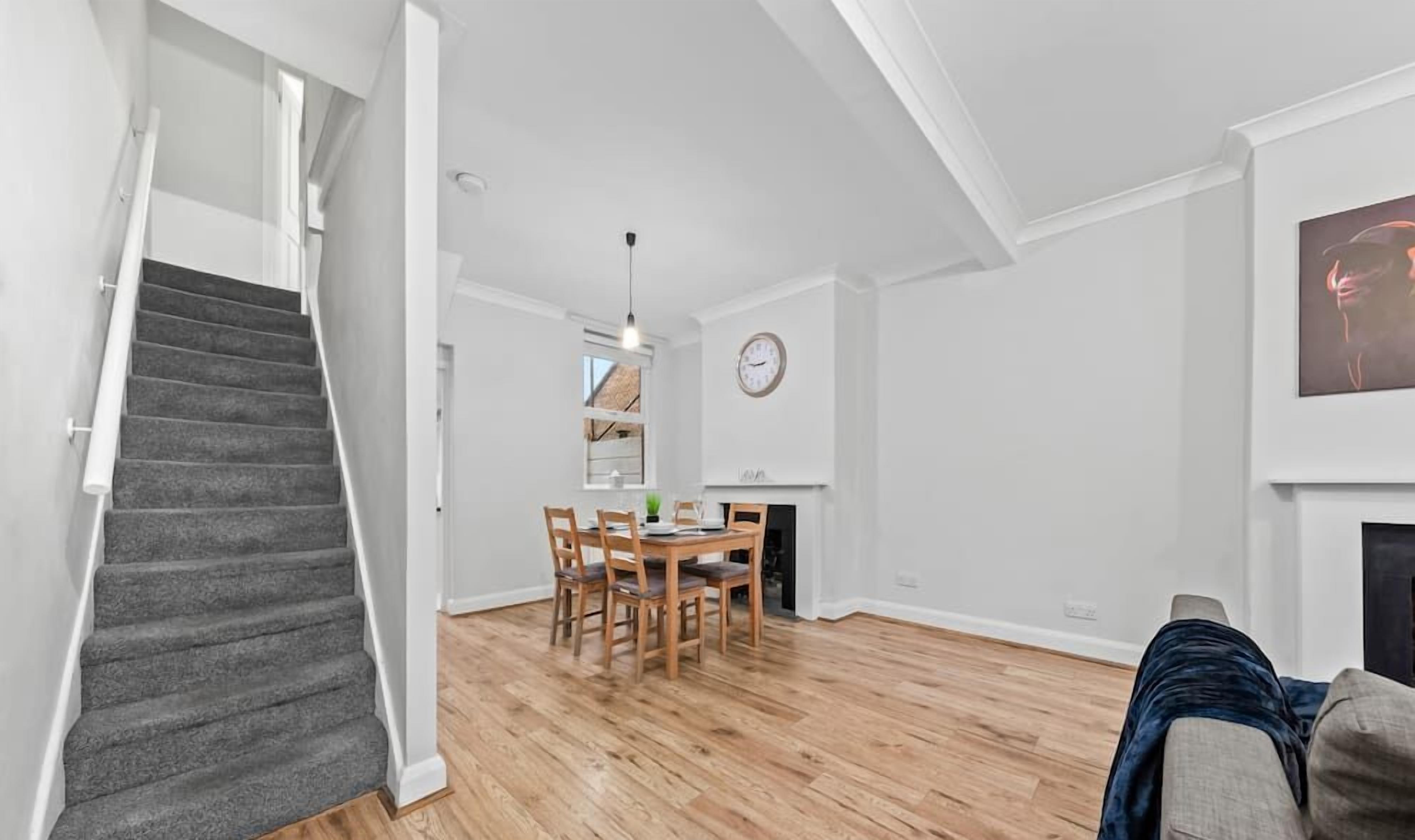 Un vaste espace de vie comprenant un escalier, une table à manger avec des chaises, une cheminée et une horloge murale.