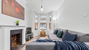 Un salon moderne avec une cheminée, un canapé gris agrémenté de coussins à motifs, une table basse et un grand tableau abstrait accroché au mur.