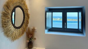 A bathroom with a round mirror, a small window with a view of the sea, and a white vanity. - Faragas Hill Oasis Villa (Aliki)