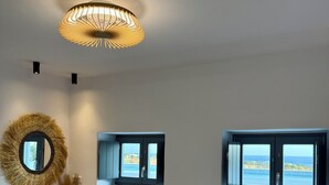 A bedroom with a bed, a round mirror, a vase with flowers, and two windows with a view. - Faragas Hill Oasis Villa (Aliki)