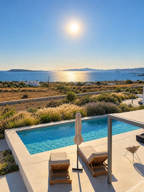 A swimming pool with lounge chairs and an umbrella, surrounded by landscaped greenery and a view of the sea. - Faragas Hill Oasis Villa (Aliki)