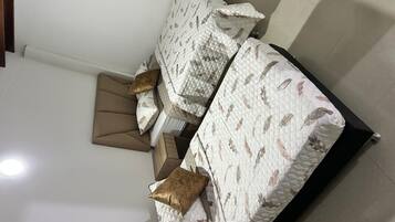 Un lit avec une couvre-lit à motifs et des oreillers, une tête de lit en bois et un mur de couleur claire.