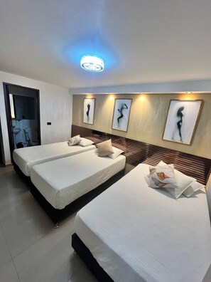 Habitación de hotel con dos camas, cabecero de madera, baño visible a través de una puerta abierta y cuadros colgados en la pared.