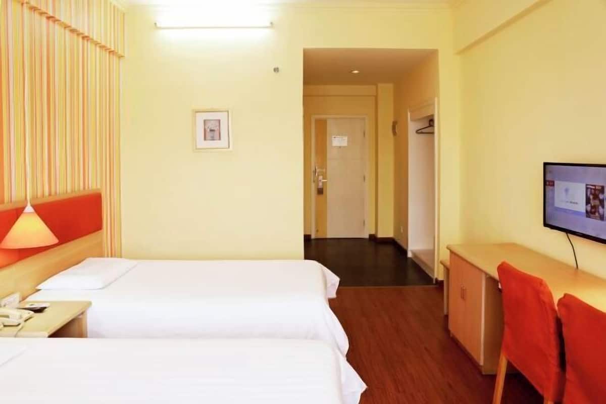 Habitación de hotel con dos camas, un escritorio, una silla, un televisor y una puerta que da a otra habitación.