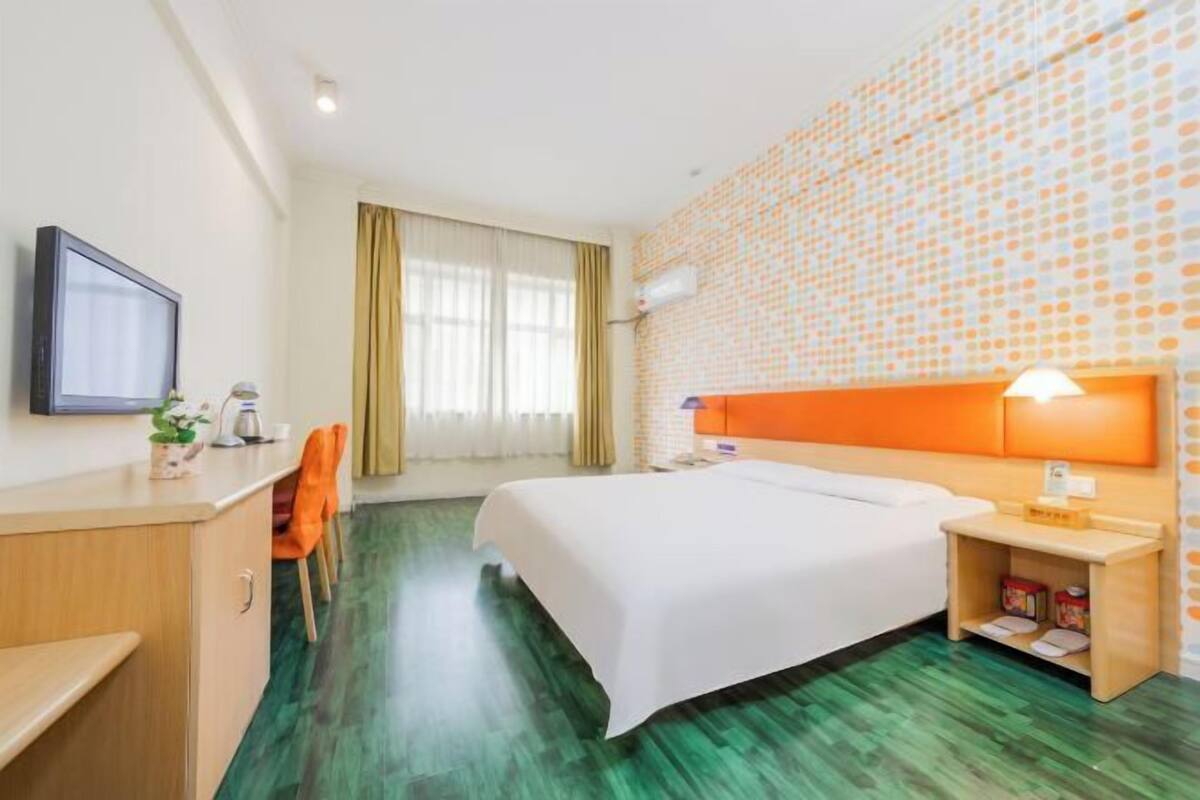 Habitación de hotel con cama, escritorio, silla, televisor y pared con estampado de lunares.
