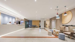 A modern hotel lobby with a reception desk, seating area, and a large wall with a circular design. - Homeinn · neo (Hangzhou Xiaoshan Train South Station Tonghuizhong Road Subway Station) (Hangzhou)