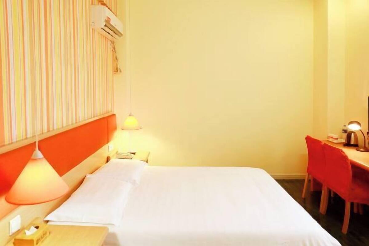 Una habitación de hotel con cama, escritorio, silla, lámpara y aire acondicionado.