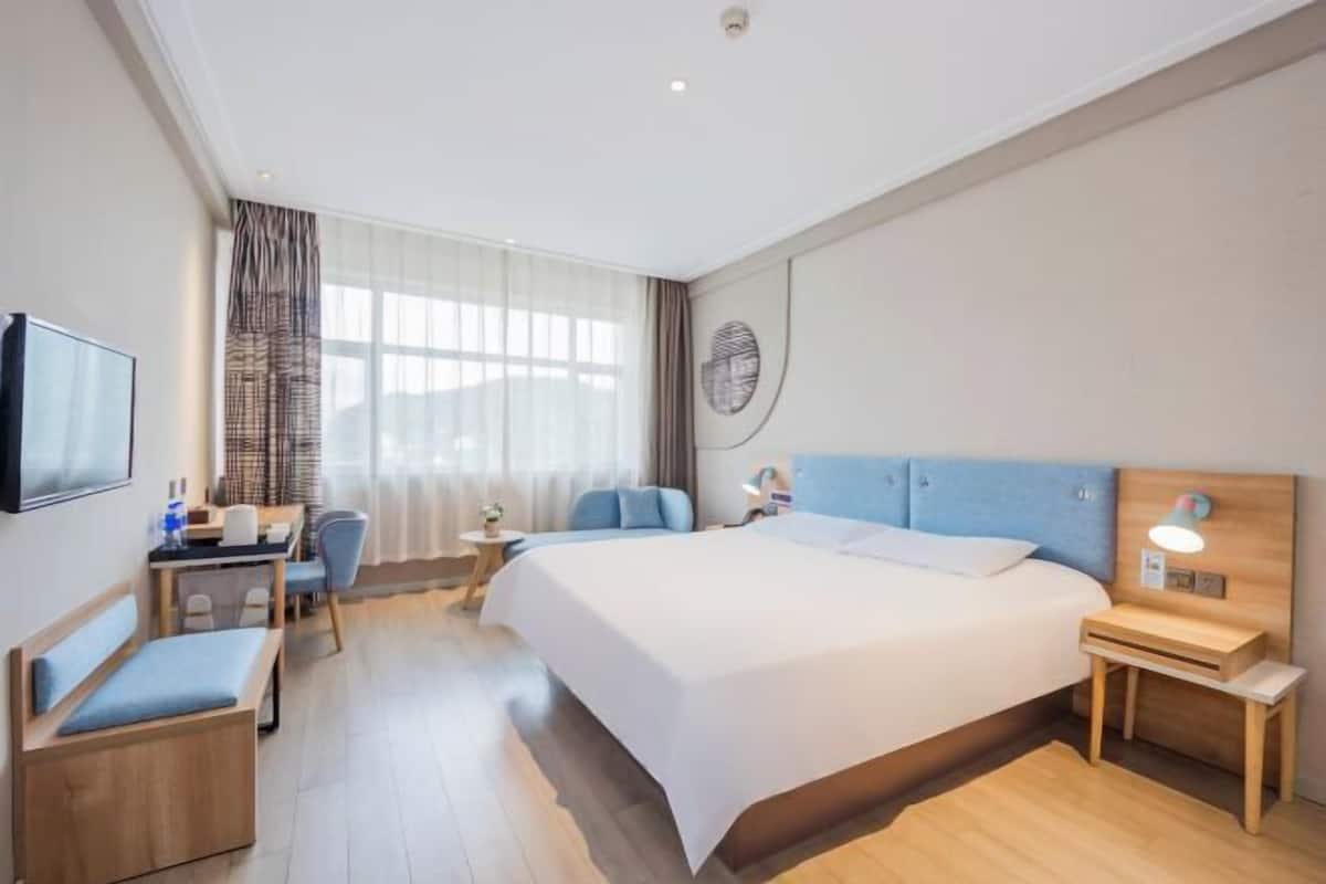 Habitación de hotel con una cama grande, un escritorio con silla, un televisor y una ventana con cortinas.