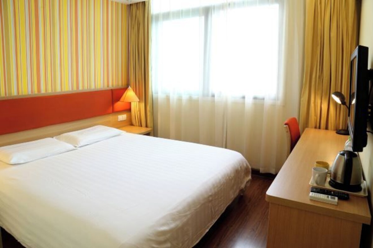 A hotel room with a large bed, a desk with a coffee maker, a television, and a window with curtains.