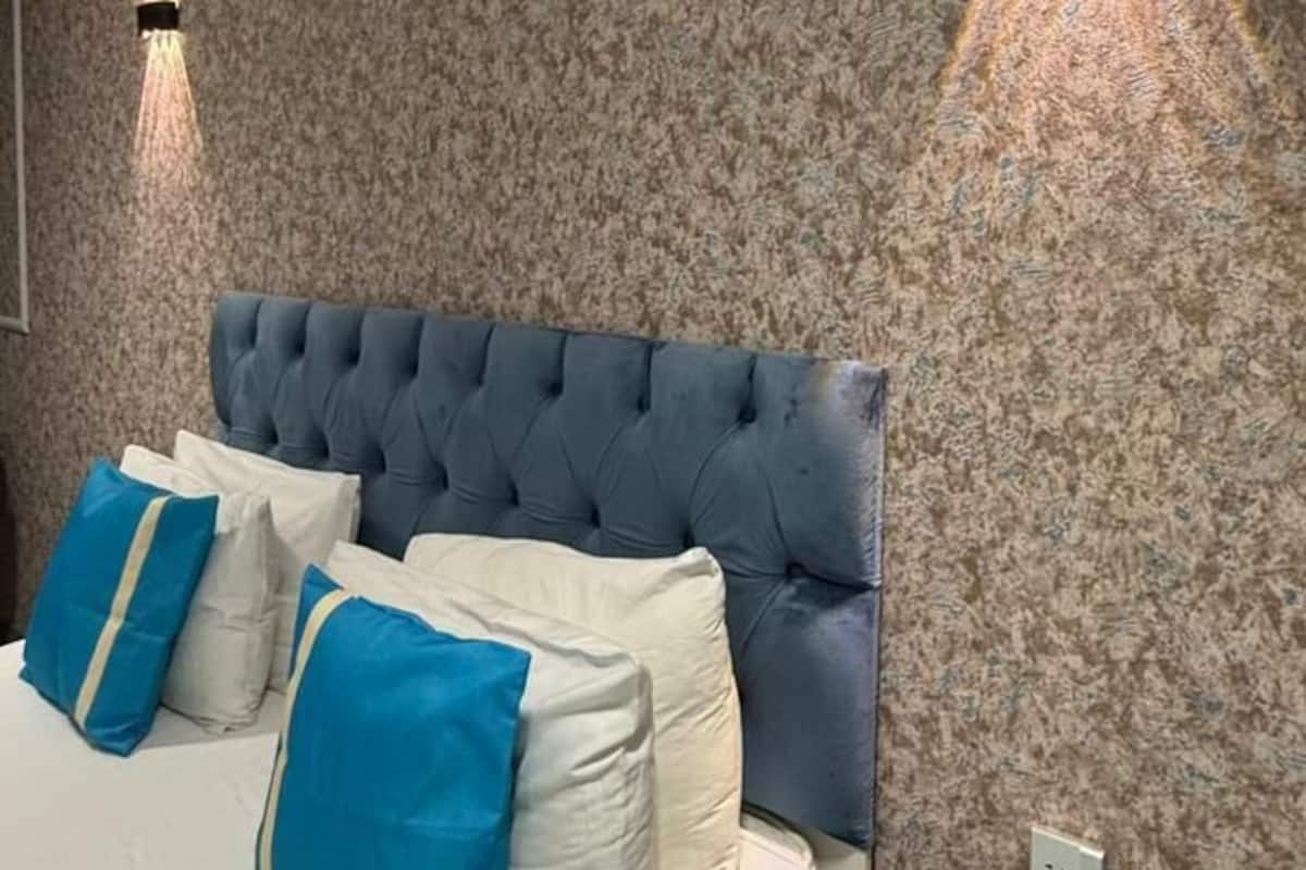 A bedroom with a tufted headboard, a bed with white and blue bedding, and two wall-mounted light fixtures.