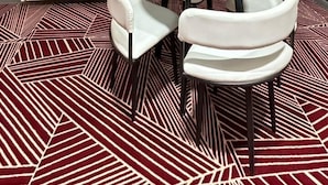 Una habitación moderna con una mesa redonda y sillas blancas tapizadas, una alfombra estampada y dos lámparas de pared.