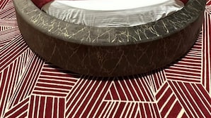 Una cama redonda con un edredón rojo, dos almohadas con estampados multicolores y un cabecero oscuro con dos luces fijadas a la pared.
