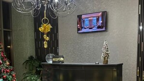 Un vestíbulo moderno con un mostrador de recepción, una lámpara de araña grande, una pantalla de televisión y un árbol de Navidad.