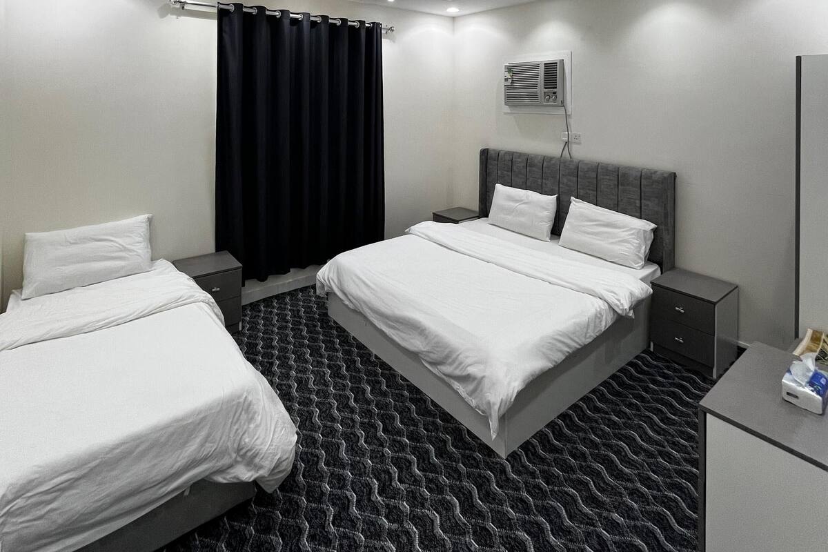 Ein modernes Hotelzimmer mit einem großen Bett, zwei Nachttischen, einem kleinen Schreibtisch, einem Spiegel und einem schwarz-weißen Teppich.
