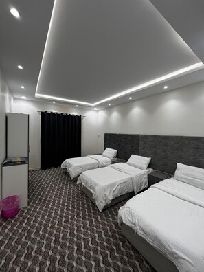 Ein modernes Hotelzimmer mit drei Einzelbetten, einem Kleiderschrank, einem Schreibtisch und einem gemusterten Teppich.