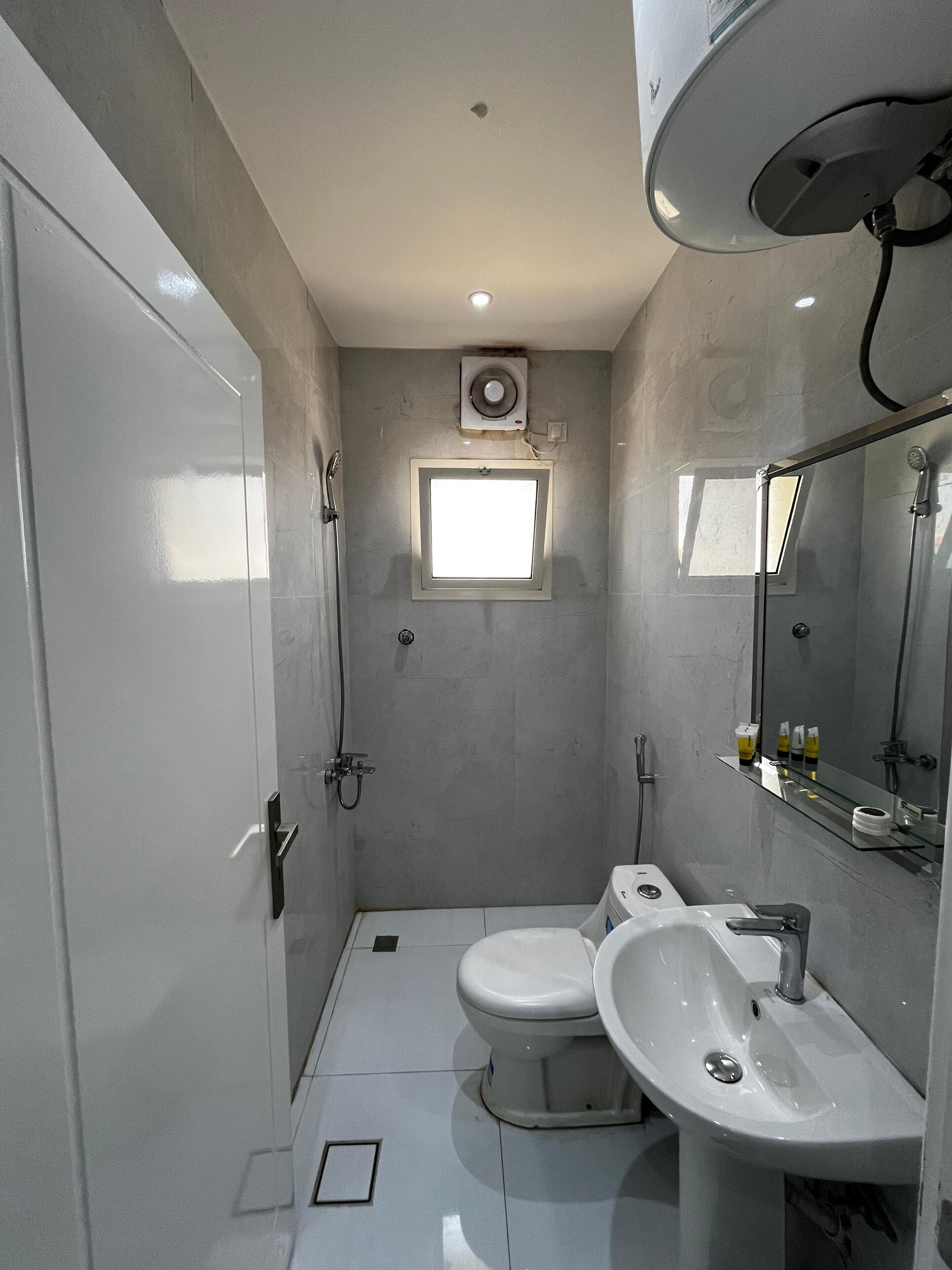 Une petite salle de bain comprenant des toilettes, un bidet et un lavabo, une petite fenêtre et un ventilateur de plafond.