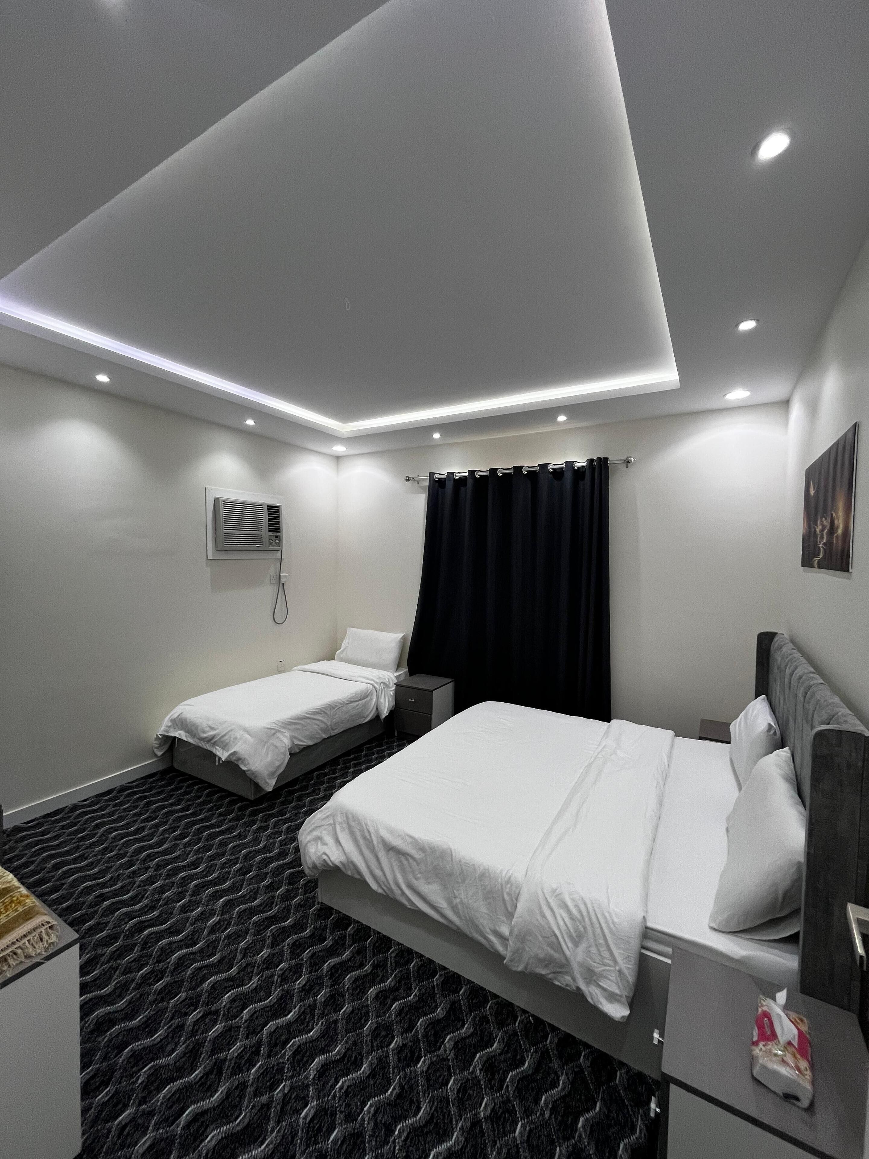 A modern hotel room with two beds, a dark patterned carpet, and recessed ceiling lighting.