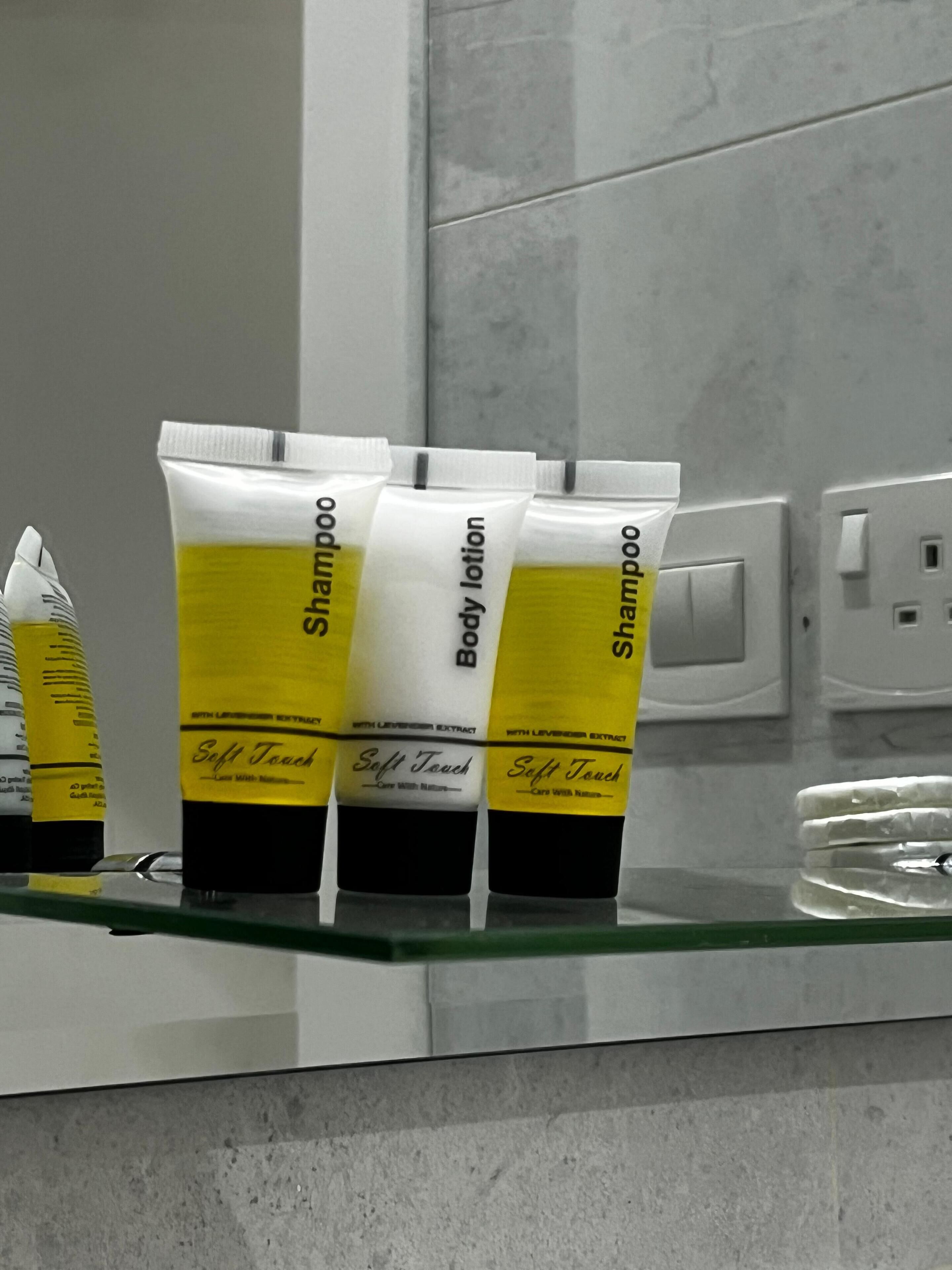 Three toiletries on a glass shelf in a bathroom.