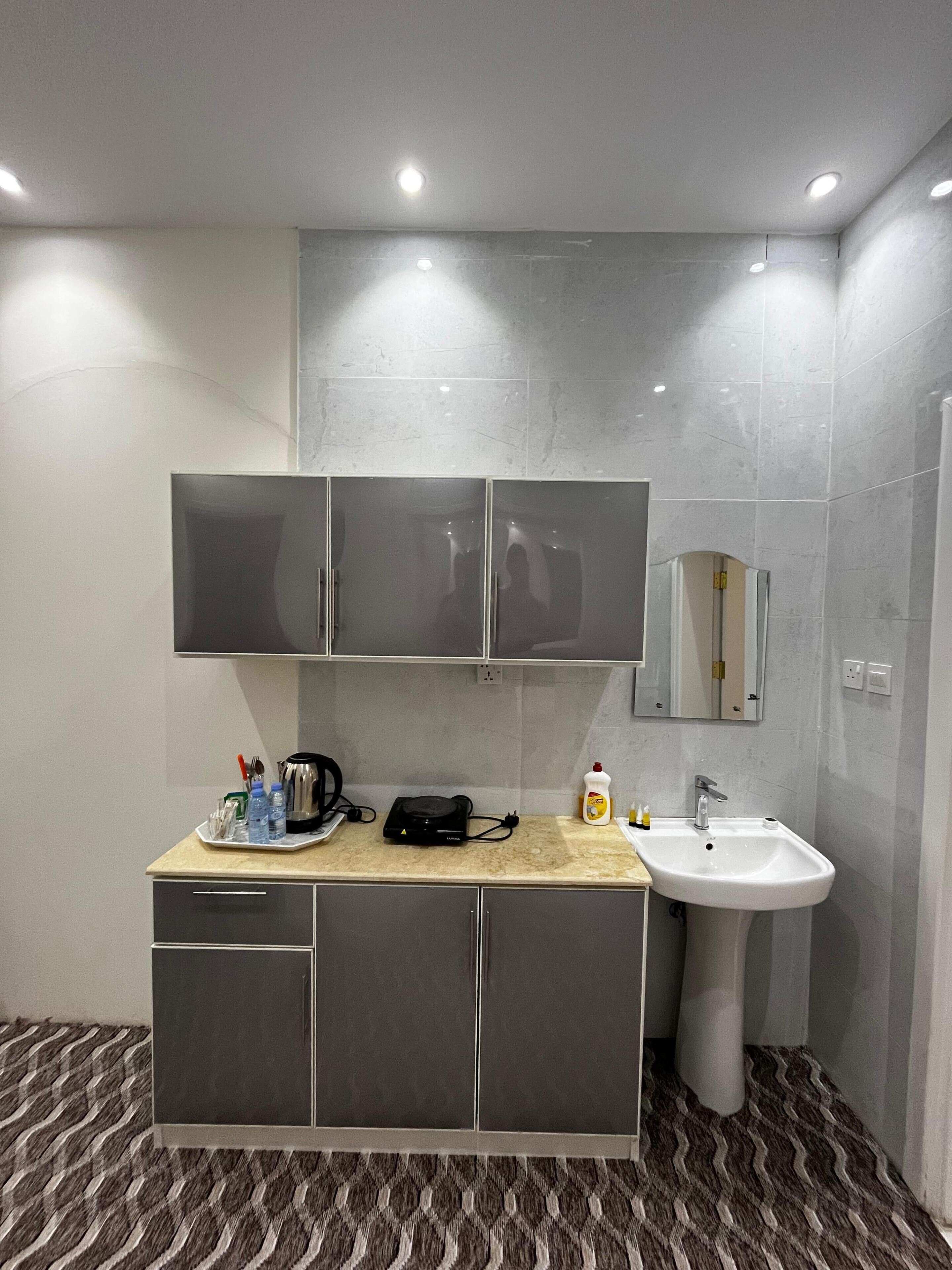 A modern bathroom with a grey cabinet, a sink, and a mirror. There are toiletries on the counter.