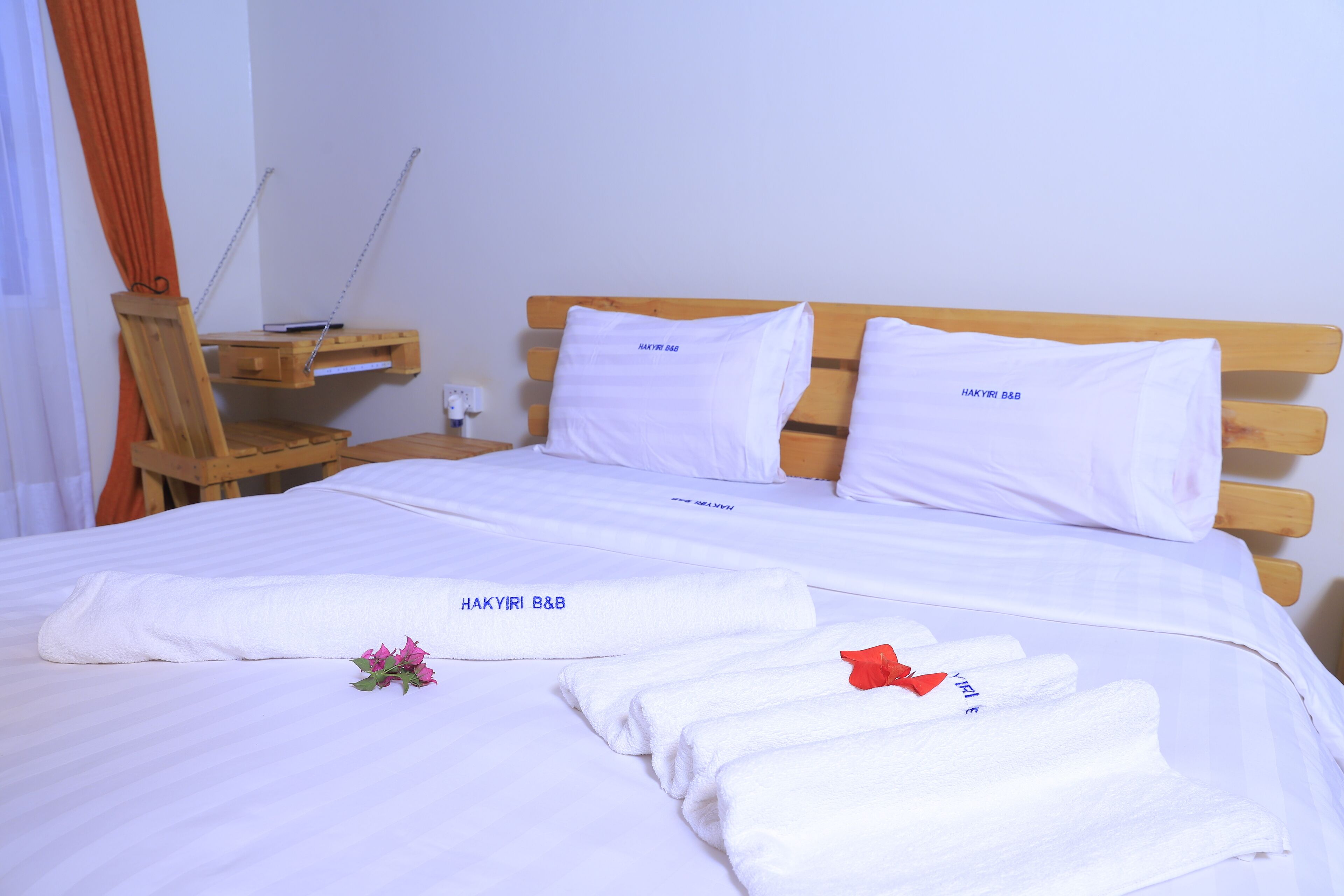 A neatly made bed with white linens, pillows, and towels, each labeled "HAKYIRI B&B".