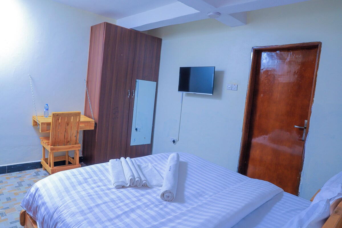 A hotel room with a bed, a wooden desk, a television, and a door.