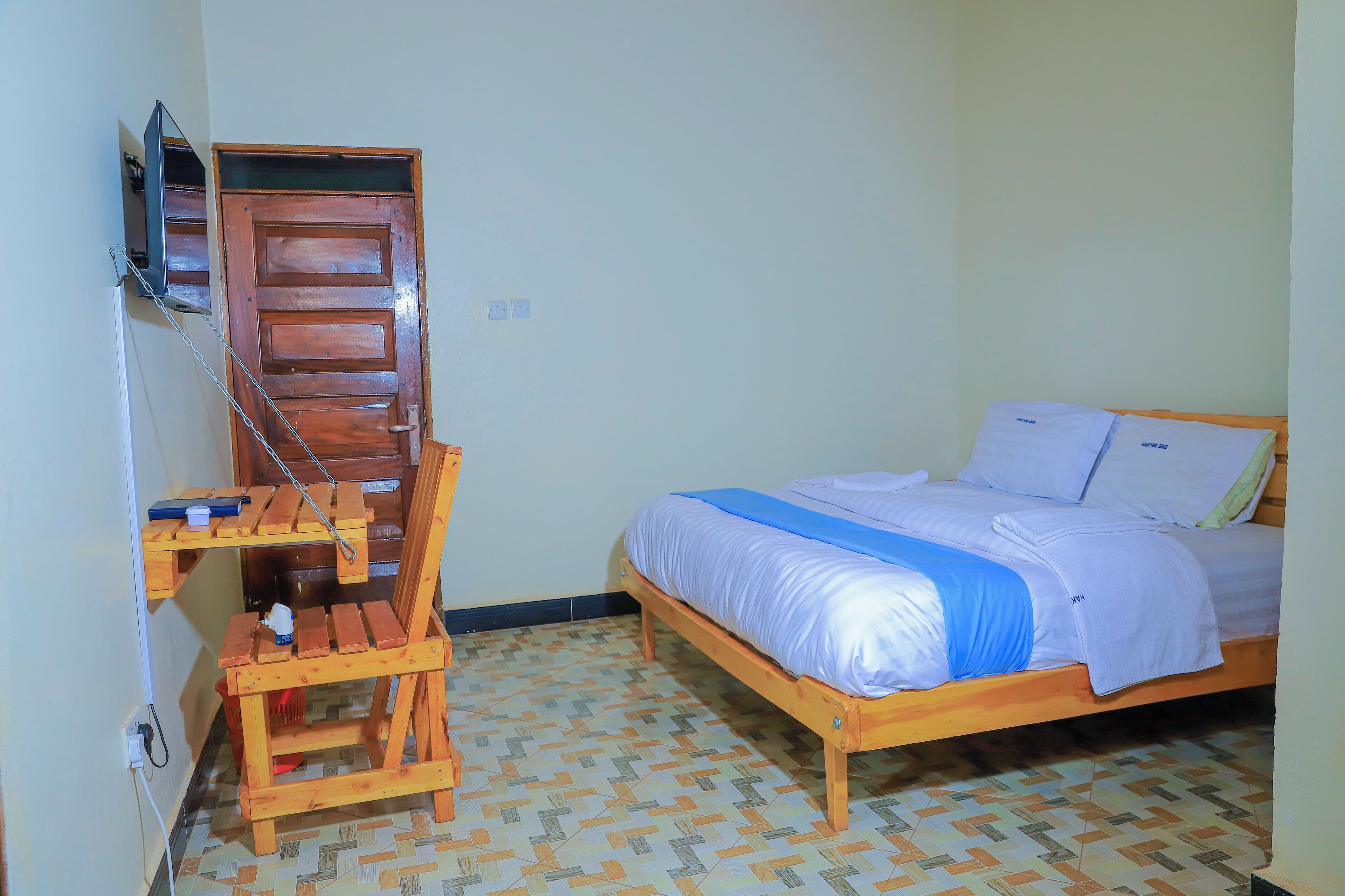 A bedroom with a wooden bed, a desk with a chair, and a television mounted on the wall.