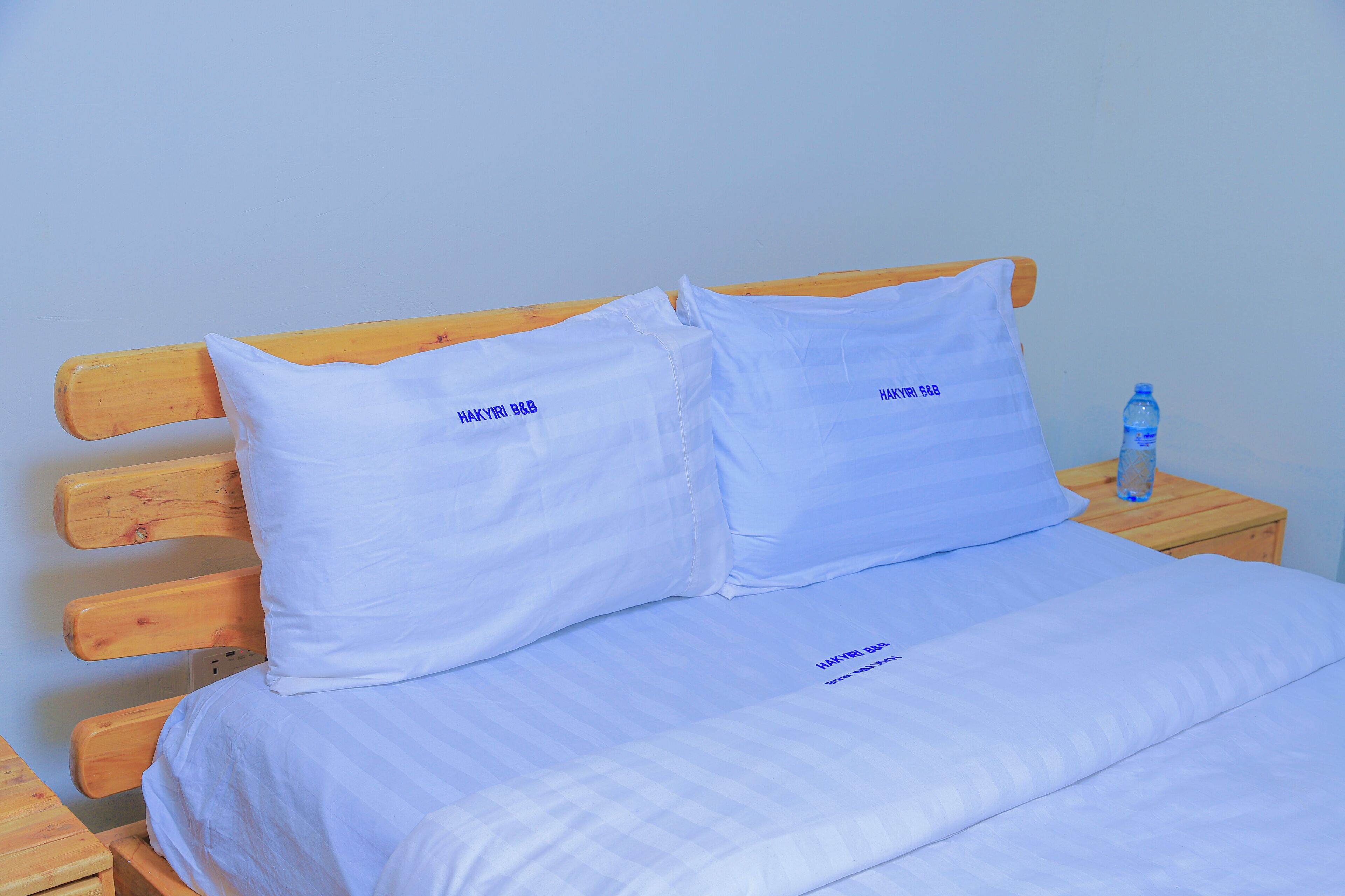 A bed with white bedding and pillows, a wooden headboard, and a wooden nightstand with a water bottle.