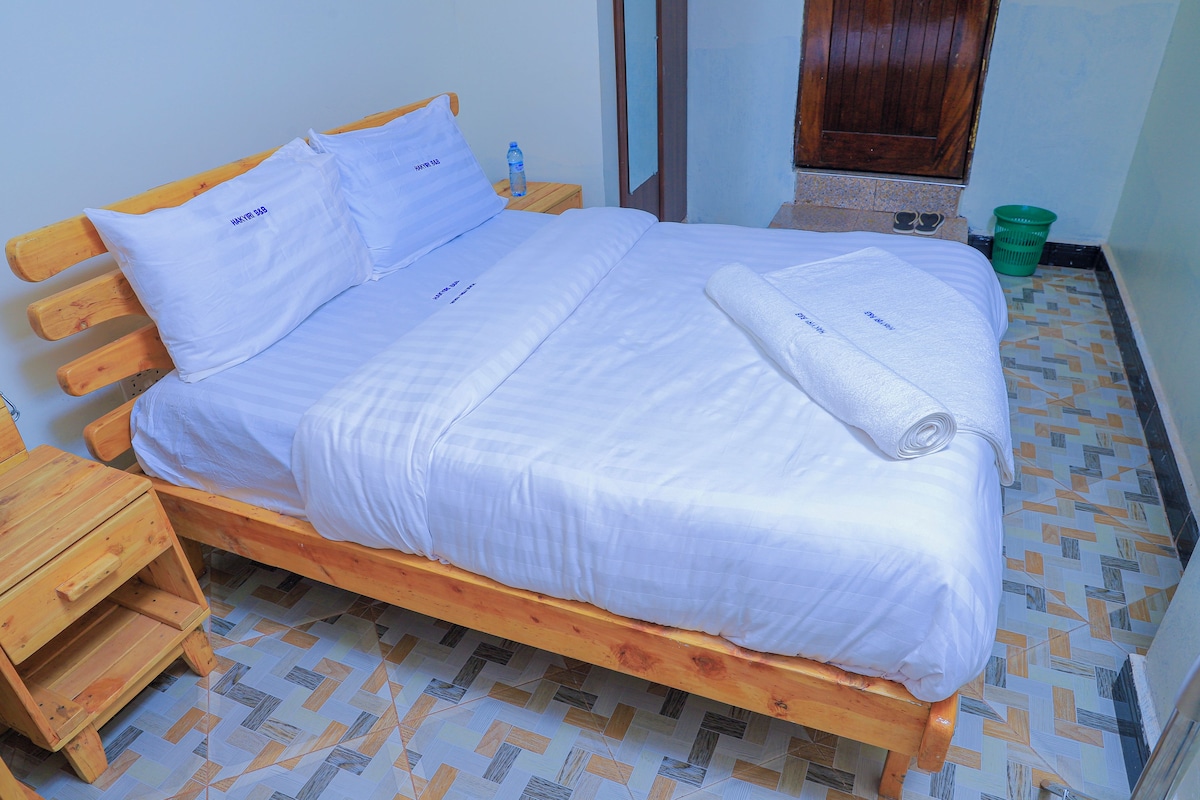 A wooden bed with white bedding, a wooden nightstand, and a green basket.