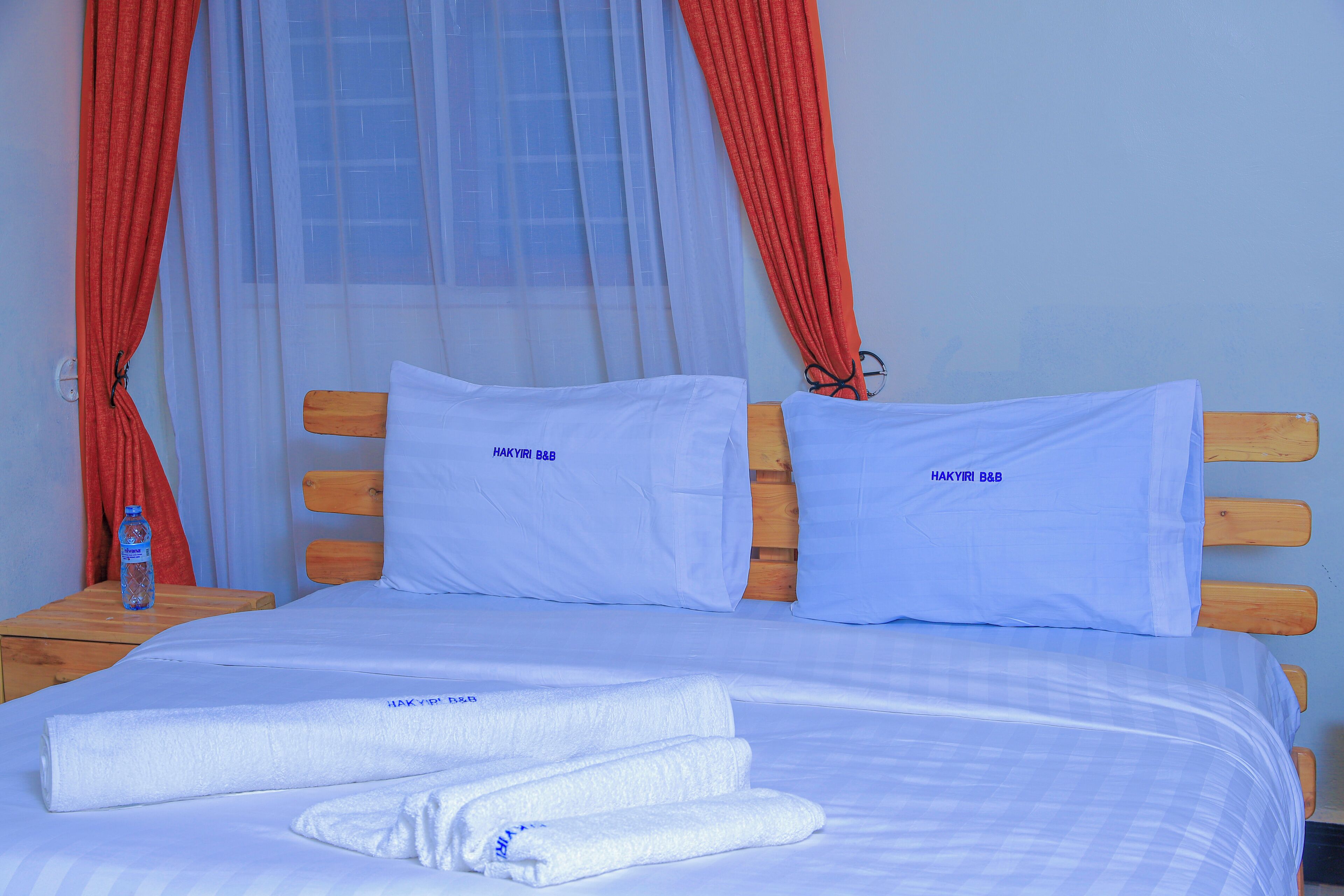 A neatly made bed with white linens and pillows, a wooden headboard, and a bottle of water on the nightstand.