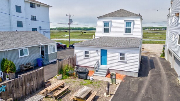 A two-story white house with a blue door, a fenced backyard, and a gravel driveway. - Oceanfront suite for 2 (Hampton)