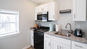 A modern kitchen with white cabinets, a black stove, a microwave, a sink, and a toaster. - Oceanfront suite for 2 (Hampton)