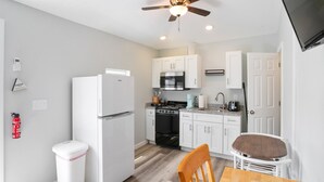 A compact kitchen with white cabinets, a black stove, and a wooden dining table with a chair. - Oceanfront suite for 2 (Hampton)