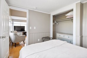Une chambre à coucher comprenant un lit, une chaise, un téléviseur et un placard avec une tringle pour suspendre les vêtements.