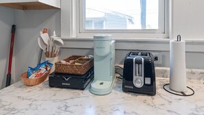 Een aanrecht met een Keurig koffiezetapparaat, een broodrooster, een mand met snacks en een keukendoekhouder.