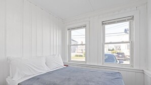 Een slaapkamer met een bed, witte muren en twee ramen.