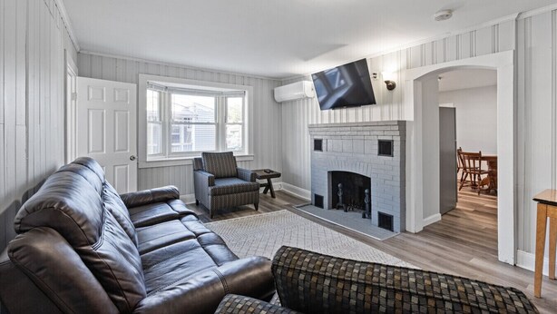 Een woonkamer met een leren bank, een gestreept fauteuil, een open haard en een flatscreen televisie erboven.