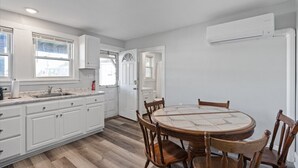 Een keuken met witte kastjes, een ronde houten tafel en een ingebouwde airconditioner.