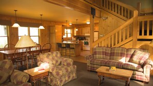 L’intérieur chaleureux d’un chalet avec des murs en bois, un coin repas, un salon doté de canapés à carreaux et une cuisine avec un îlot central.