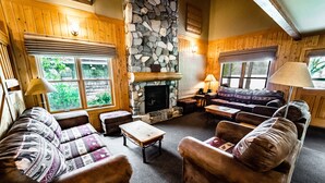 A cozy living room with a stone fireplace, wooden walls, and comfortable seating.