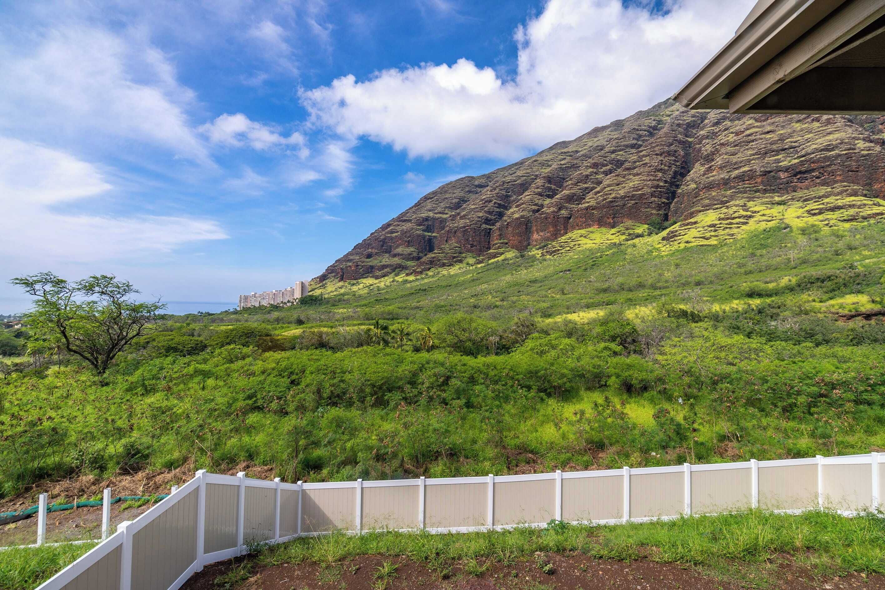 A view of a lush green landscape with a white fence and a mountain in the background.