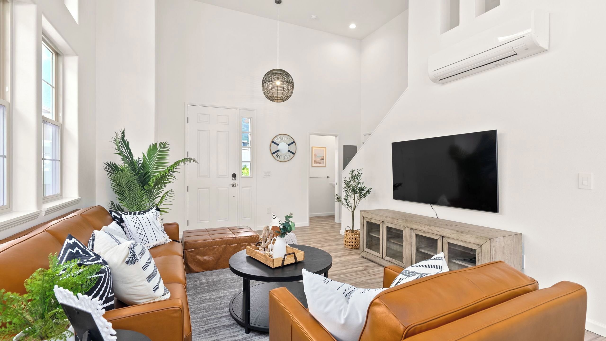 A modern living room with leather sofas, a round coffee table, a flat-screen TV, and a large window.
