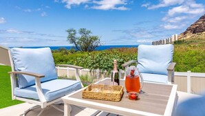 Eine Terrasse mit zwei weißen Liegestühlen, einem Tisch, einer Champagnerflasche, Gläsern und einer Trinkkaraffe.