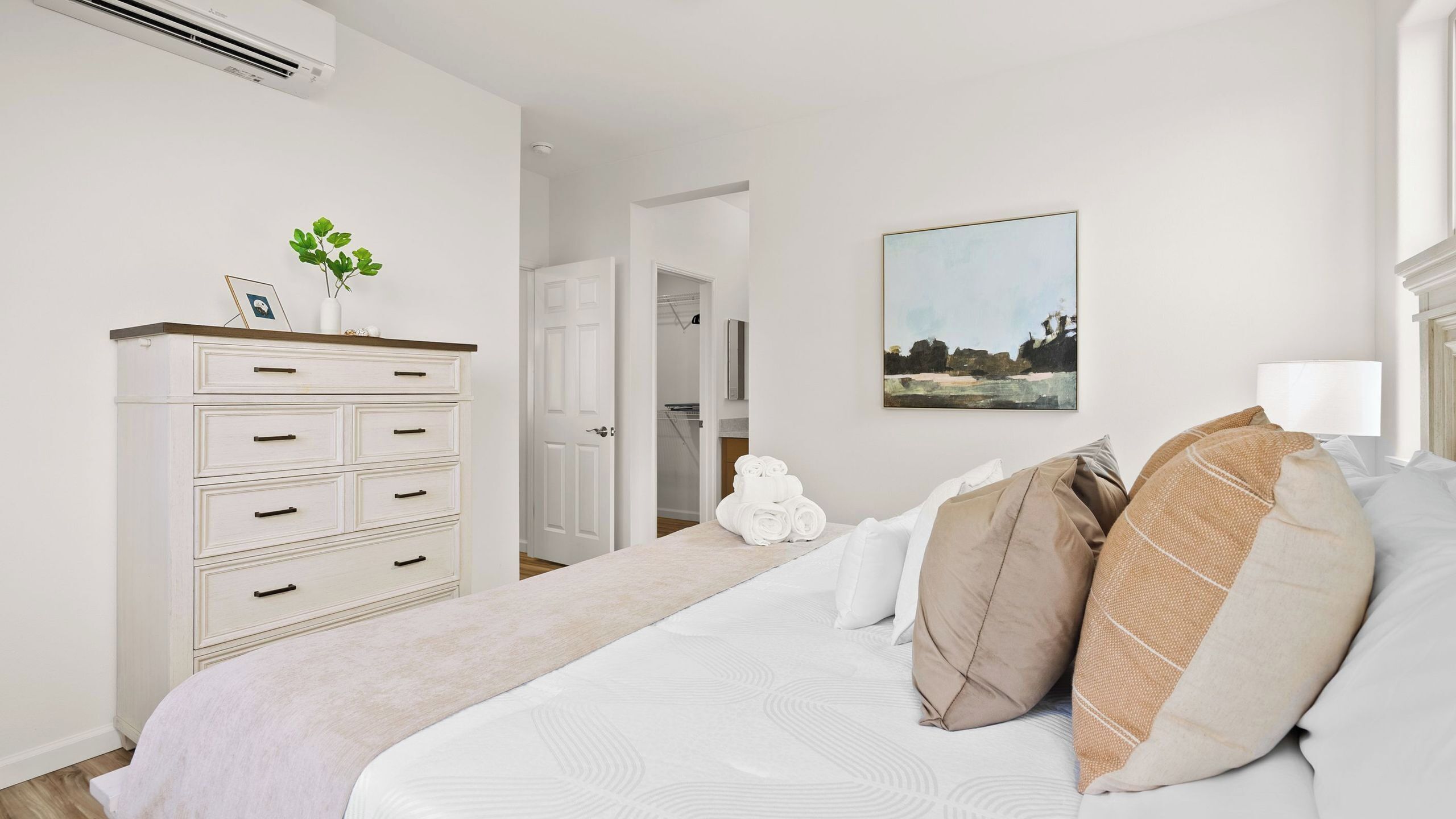 Une chambre à coucher comprenant un lit, une commode, un tableau et un couloir menant à un placard.